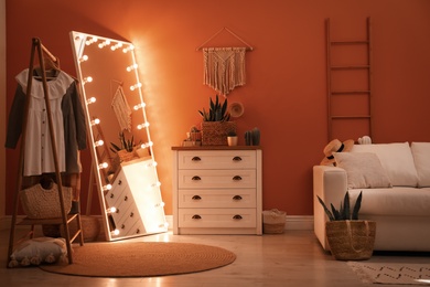 Large mirror with light bulbs and chest of drawers in stylish room interior