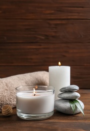 Photo of Beautiful composition with spa stones, towel and burning candles on wooden table