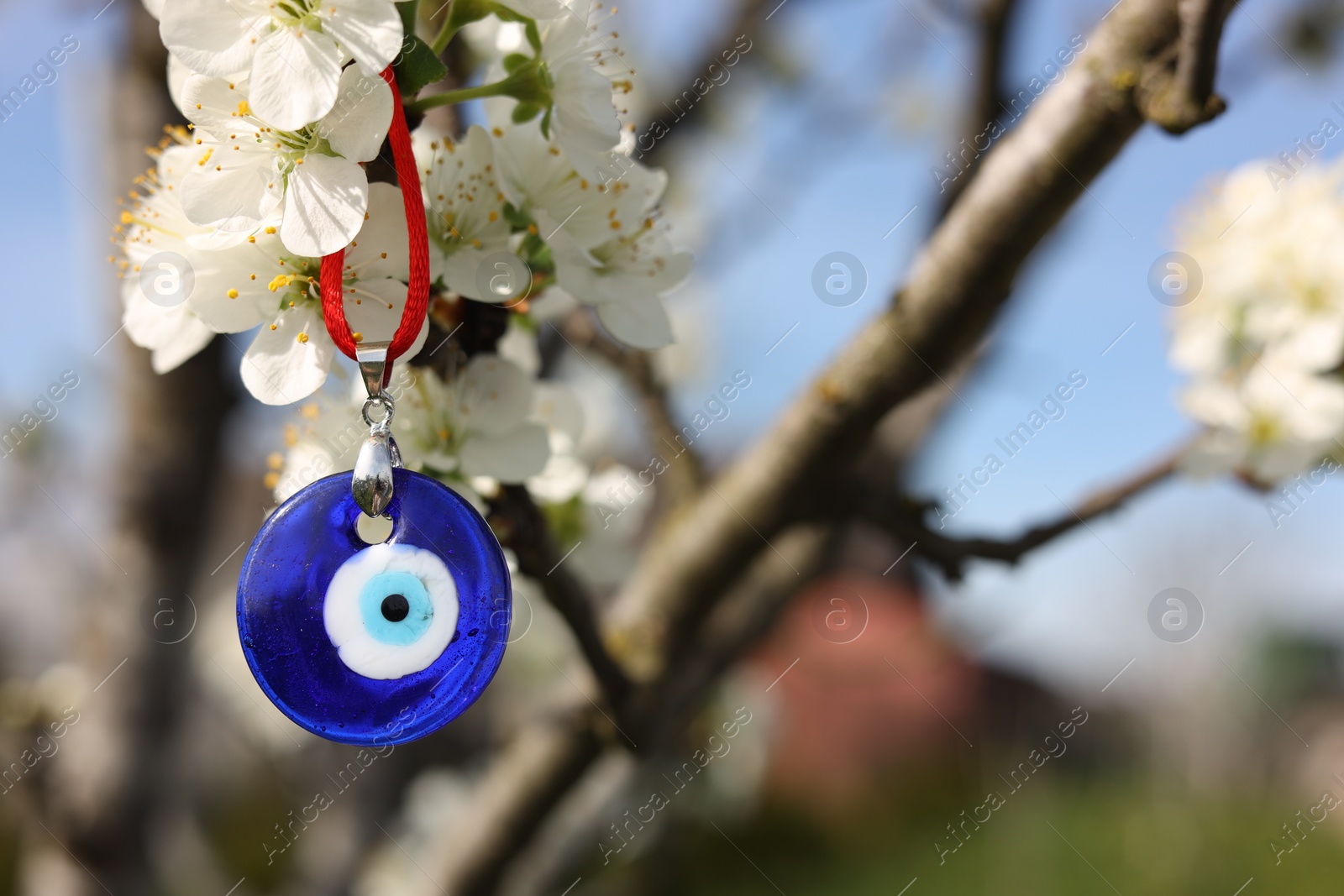 Photo of Evil eye amulet hanging on blossoming spring tree outdoors. Space for text