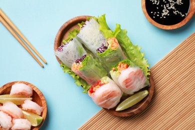 Photo of Delicious spring rolls, shrimps, lime and chopsticks on light blue background, flat lay