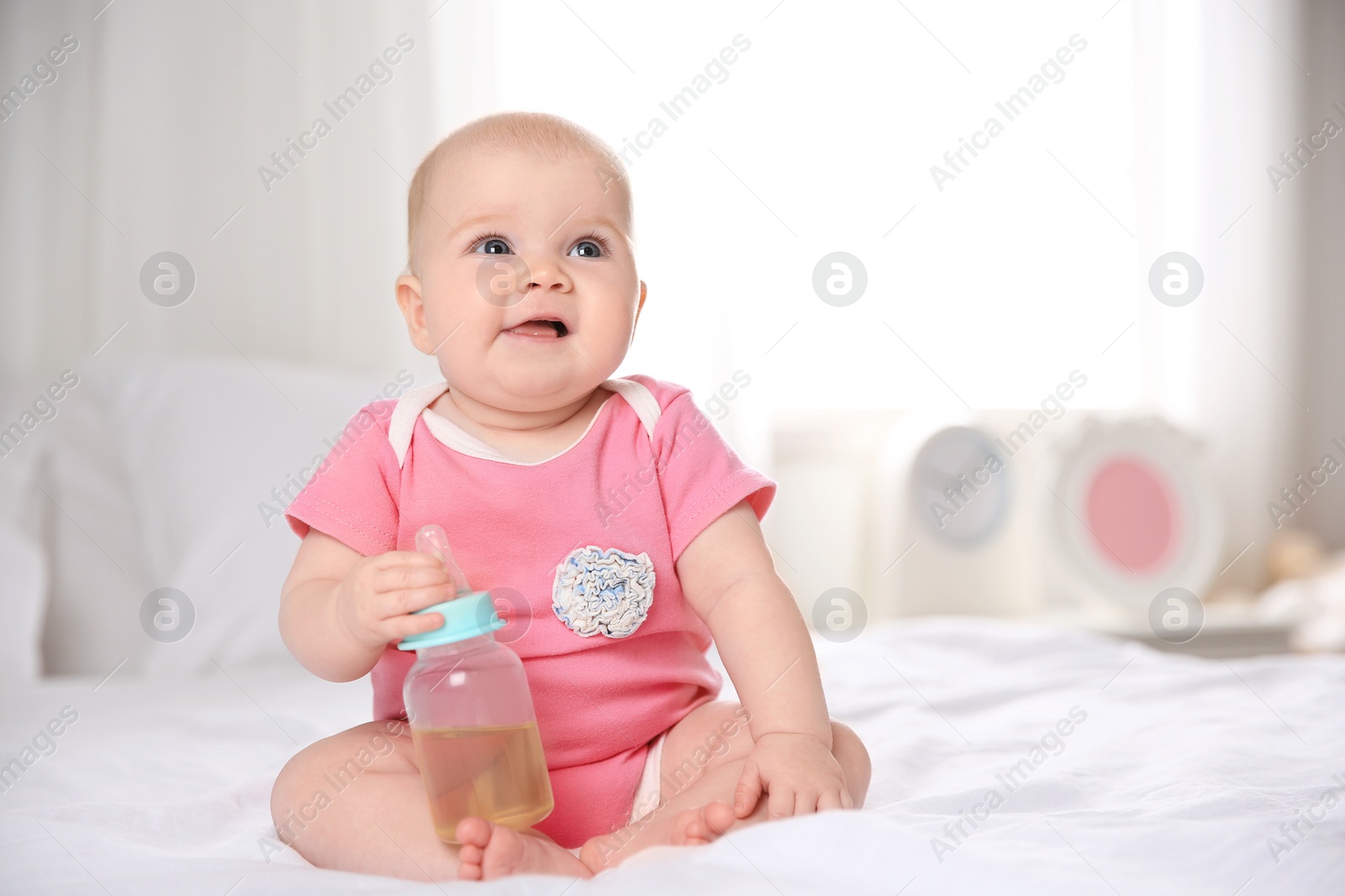 Photo of Pretty baby sitting with bottle on bed at home. Space for text