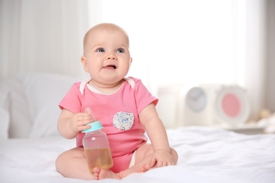 Pretty baby sitting with bottle on bed at home. Space for text