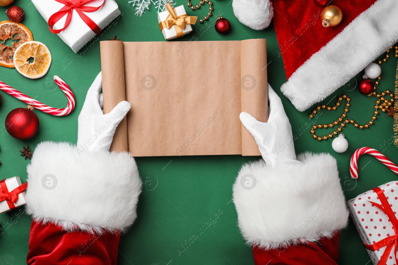 Photo of Santa Claus holding empty scroll and Christmas decor on color background, top view