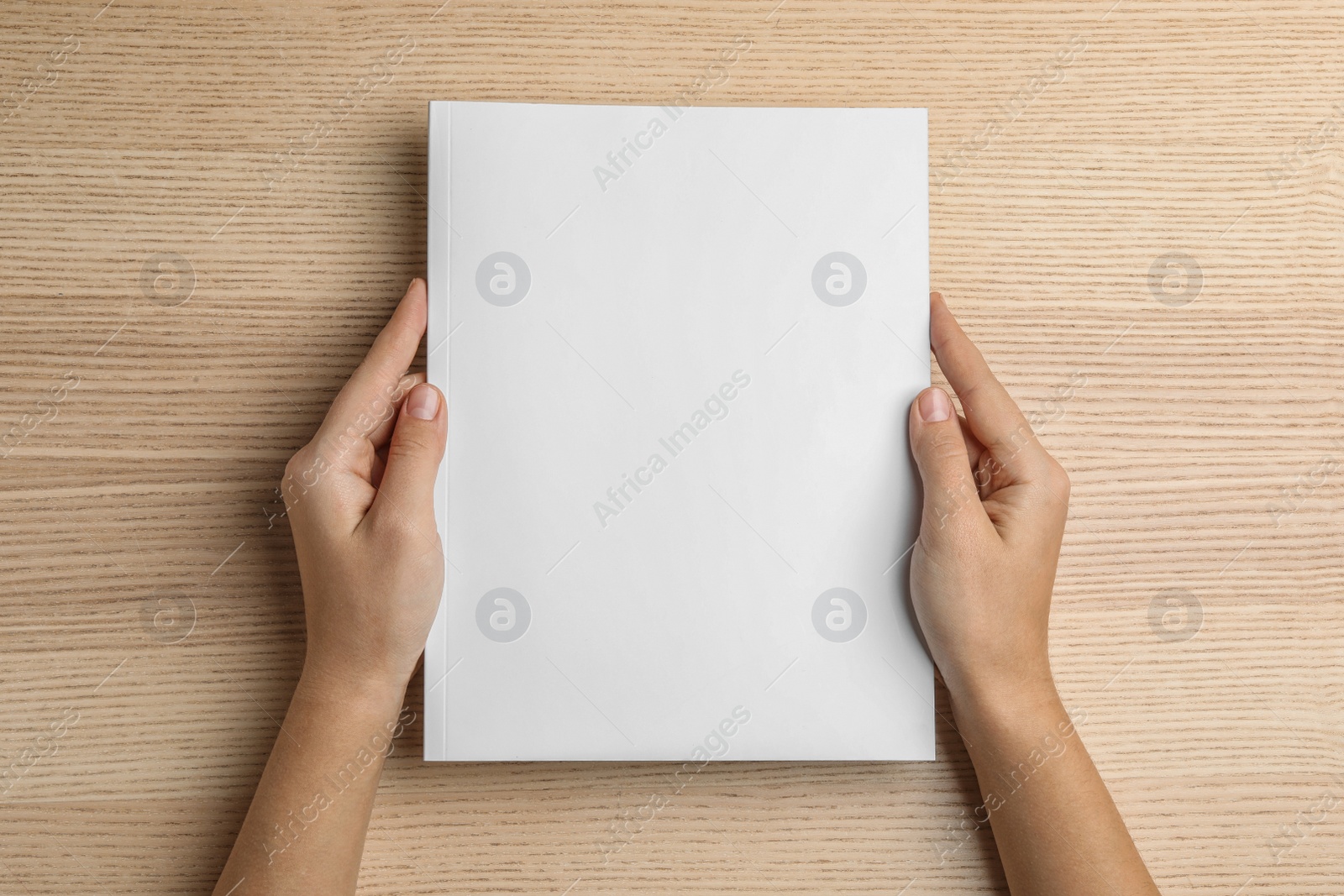 Photo of Woman holding brochure with blank cover on wooden background, top view. Mock up for design