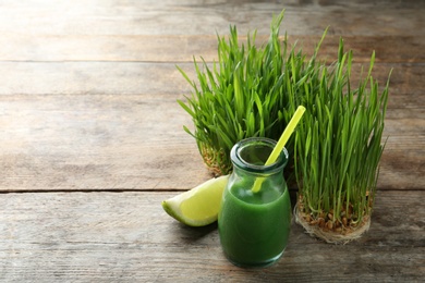 Photo of Glass bottle of wheat grass juice with citrus fruit and sprouts on wooden background. Space for text
