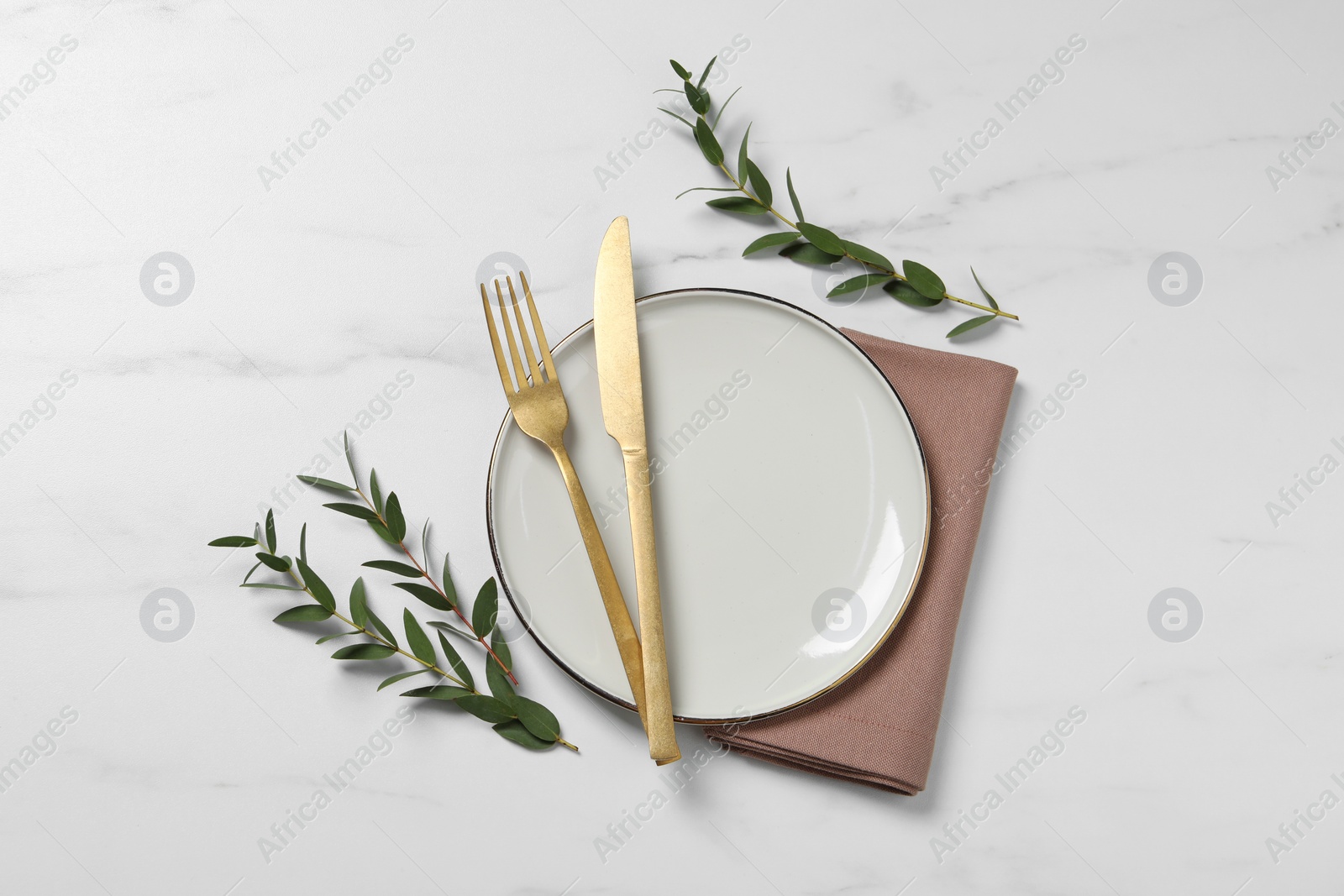 Photo of Stylish setting with cutlery and eucalyptus leaves on white marble table, flat lay