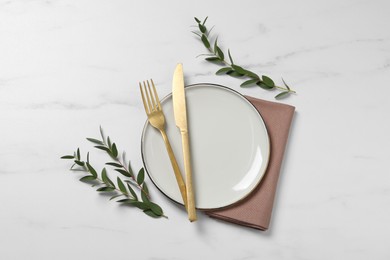 Photo of Stylish setting with cutlery and eucalyptus leaves on white marble table, flat lay