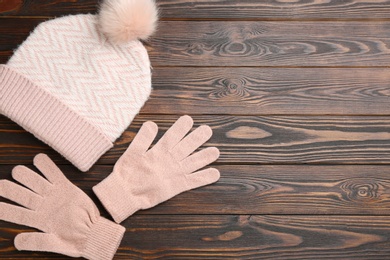 Woolen gloves and hat on wooden background, flat lay. Space for text