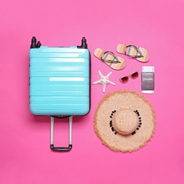 Blue suitcase and beach objects on pink background, flat lay