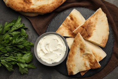 Photo of Cut pita bread, cream cheese and parsley on grey table, flat lay