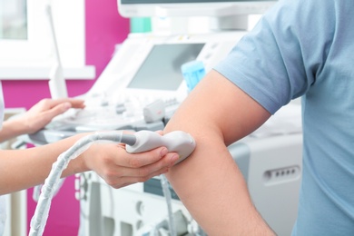 Doctor conducting ultrasound examination of elbow joint in clinic, closeup