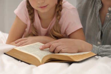 Photo of Girl and her godparent reading Bible together indoors, closeup
