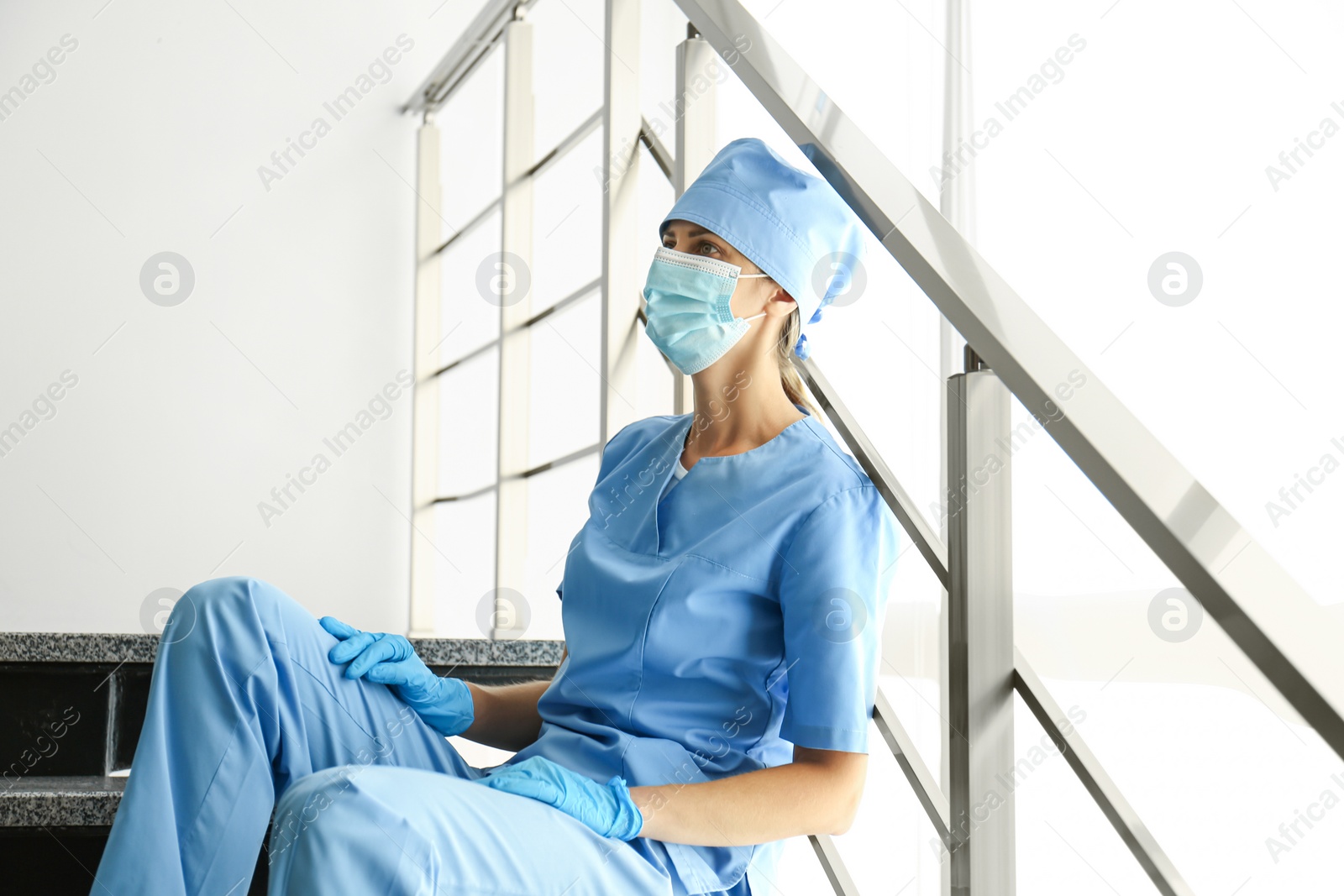 Photo of Exhausted doctor sitting on stairs in hospital. Stress of health care workers during COVID-19 pandemic