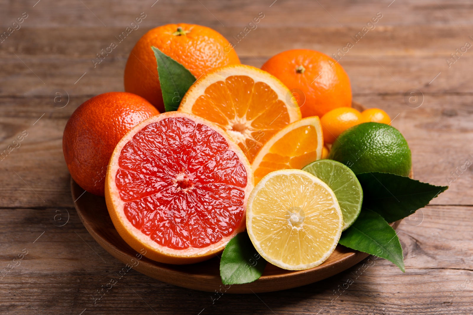 Photo of Fresh juicy citrus fruits with green leaves on wooden table