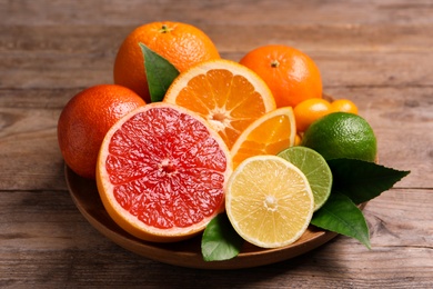 Photo of Fresh juicy citrus fruits with green leaves on wooden table