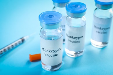 Monkeypox vaccine in glass vials and syringe on light blue background