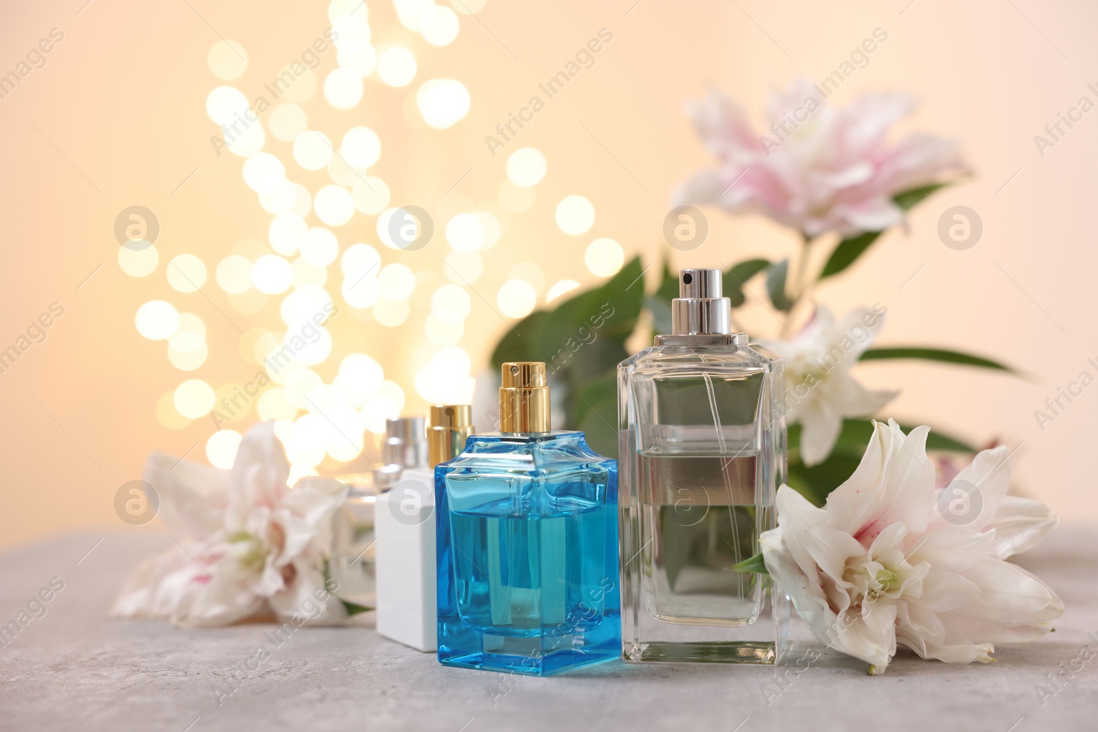 Photo of Perfume bottles and bouquet of beautiful lily flowers on table against beige background with blurred lights, closeup