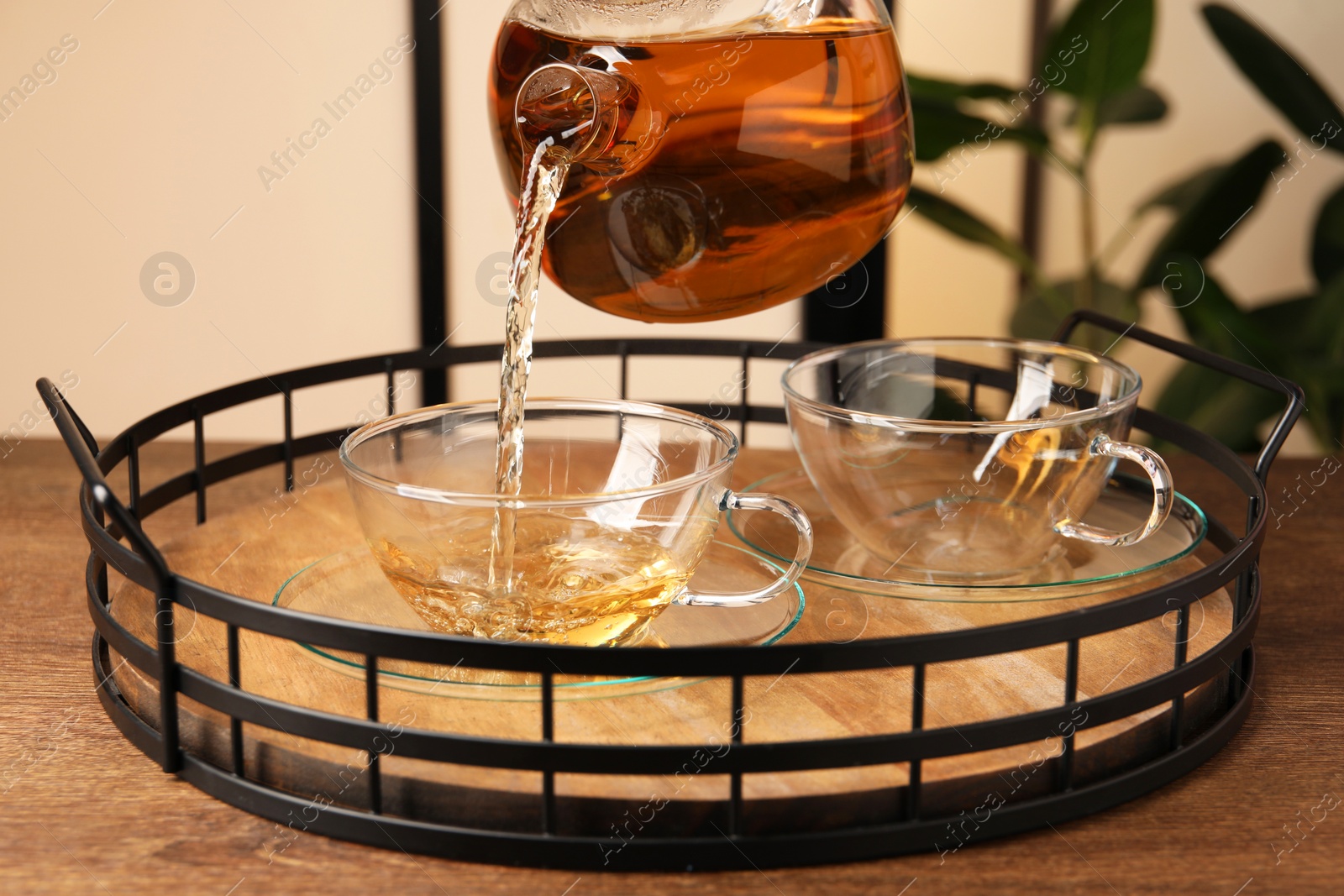 Photo of Pouring tasty tea into glass cup at wooden table, closeup