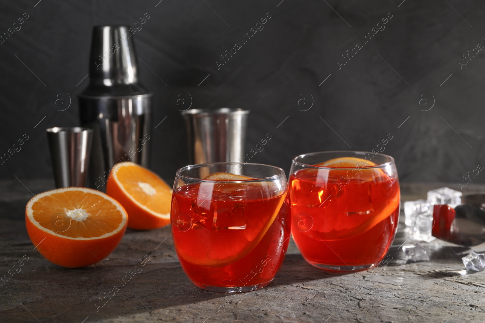 Photo of Aperol spritz cocktail, ice cubes and orange slices in glasses on grey textured table