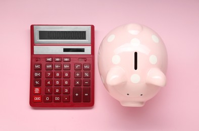Calculator and piggy bank on pink background, top view
