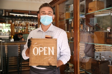 Photo of Waiter holding OPEN sign in restaurant. Catering during coronavirus quarantine