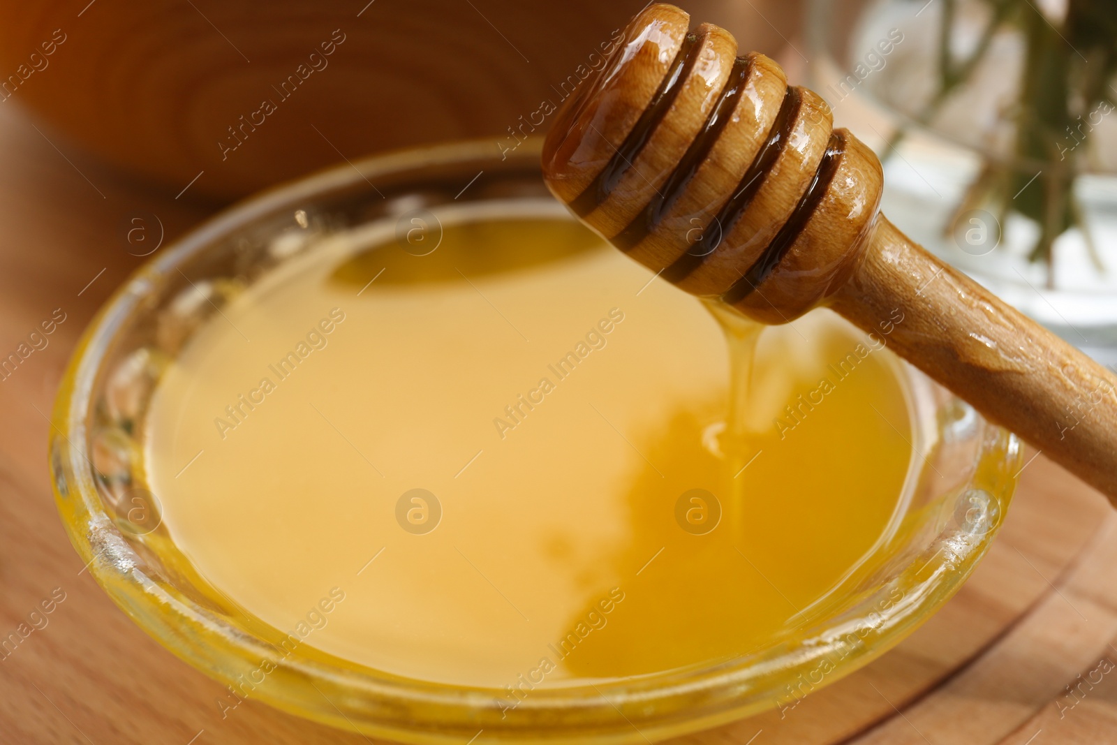 Photo of Delicious honey flowing down from dipper into bowl on wooden table, closeup