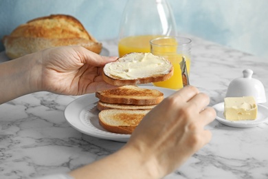 Photo of Woman spreading butter onto slice of bread over marble table, closeup