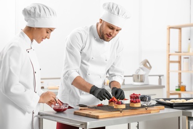 Photo of Pastry chefs preparing desserts at table in kitchen