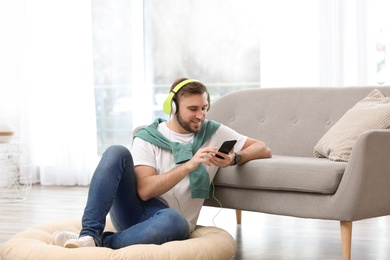 Photo of Young man with headphones and mobile device enjoying music on floor in living room