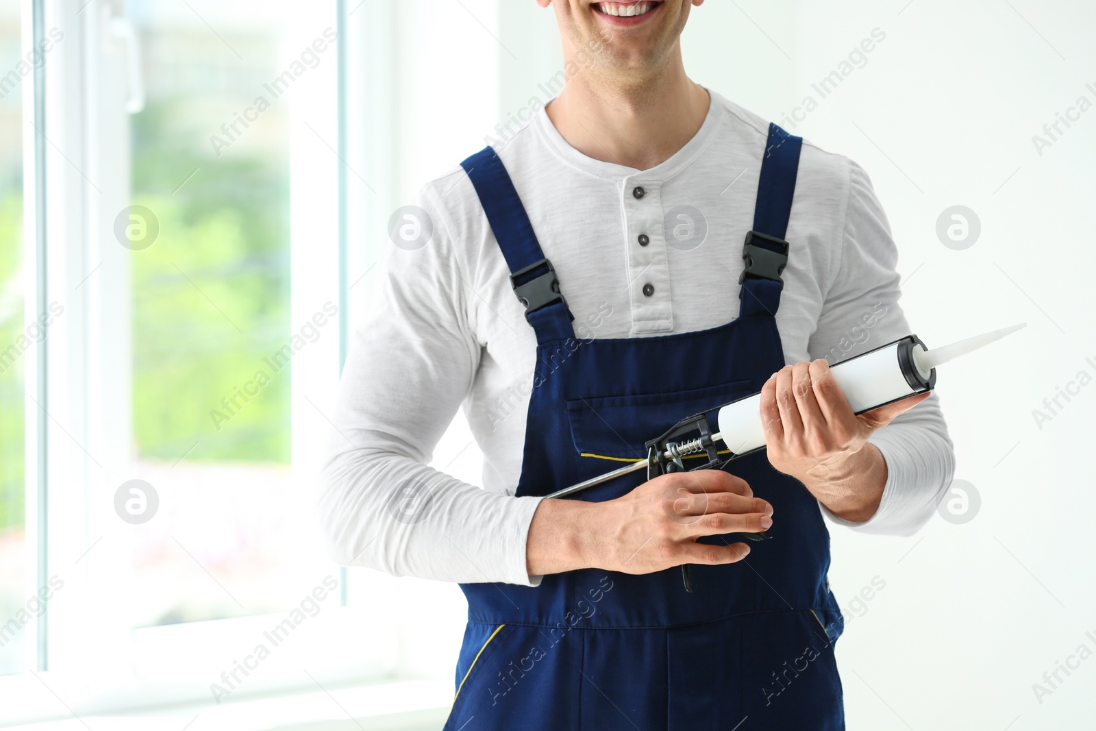 Photo of Construction worker in uniform with window sealant indoors