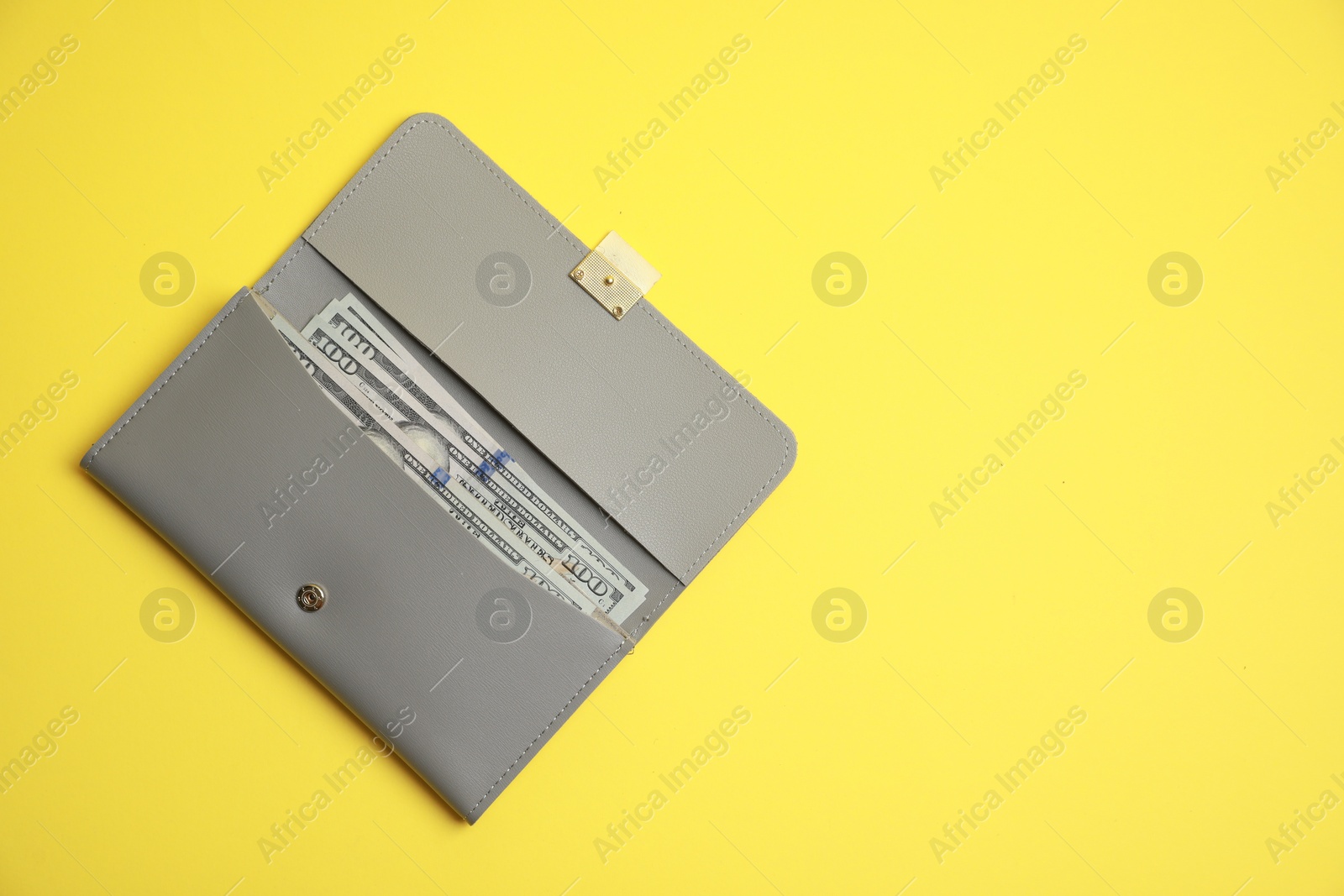 Photo of Stylish light grey leather purse with dollar banknotes on yellow background, top view. Space for text