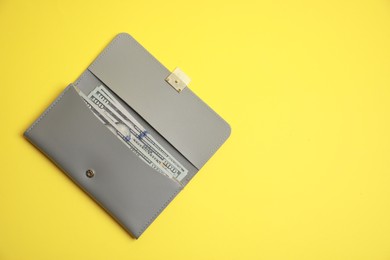 Stylish light grey leather purse with dollar banknotes on yellow background, top view. Space for text