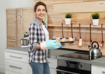 Young woman with baking sheet of cookies near oven in kitchen