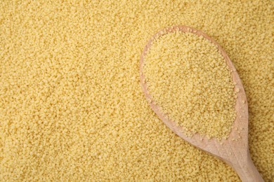 Photo of Wooden spoon and uncooked organic couscous as background, top view. Space for text