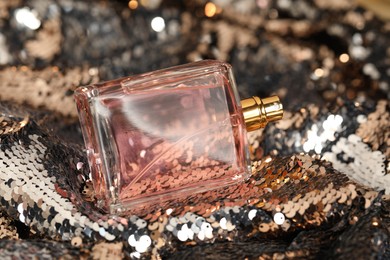 Photo of Luxury perfume in bottle on fabric with shiny sequins, closeup