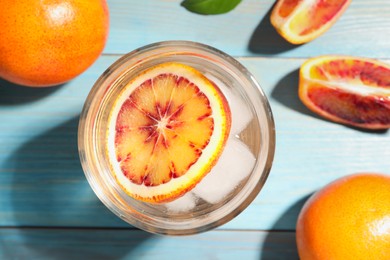 Delicious refreshing drink with sicilian orange, fresh fruits and green leaves on light blue wooden table, flat lay