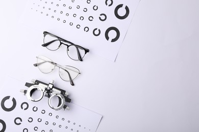 Vision test charts, glasses and trial frame on white background, flat lay. Space for text
