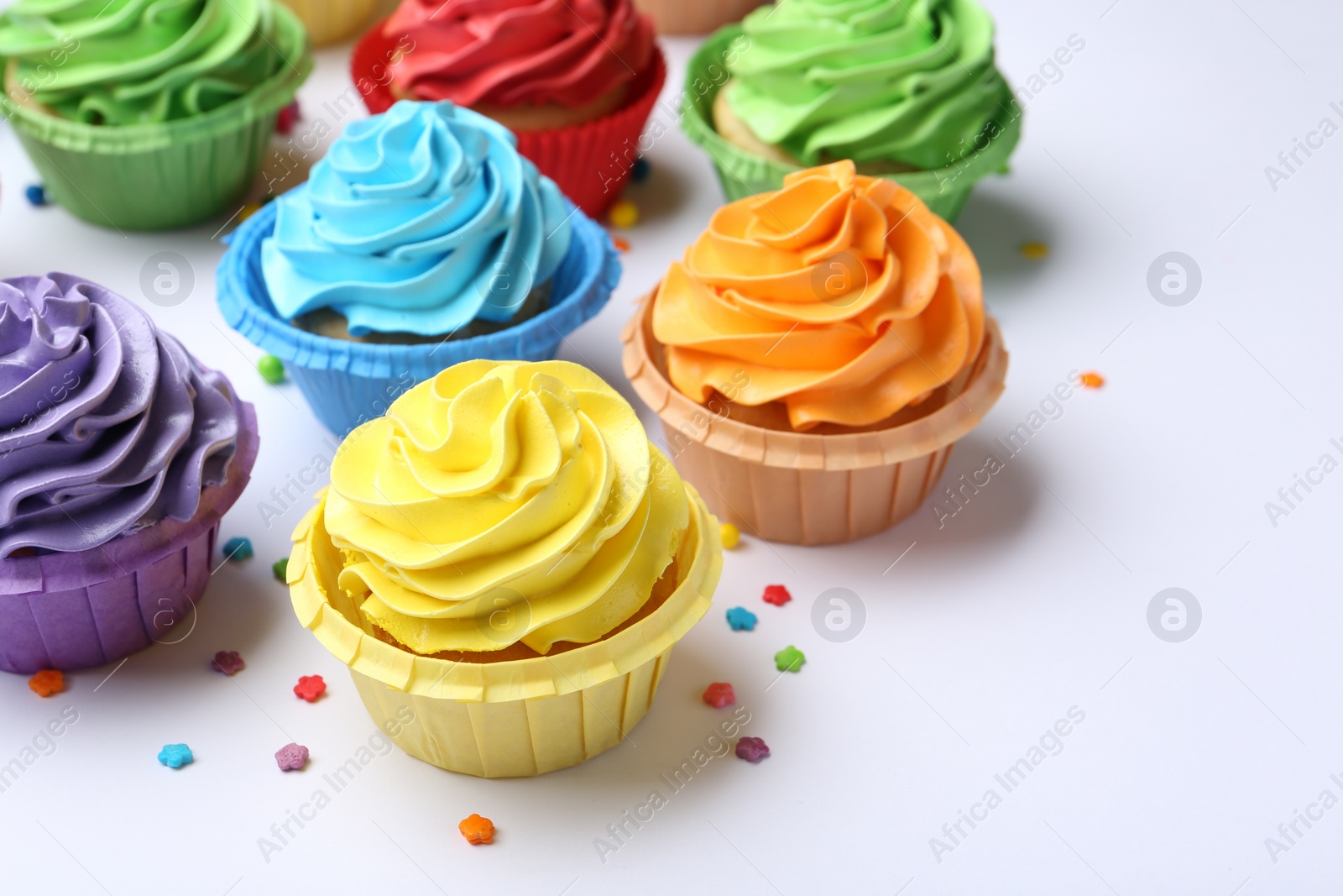 Photo of Many tasty cupcakes with bright cream and sprinkles on white background, closeup