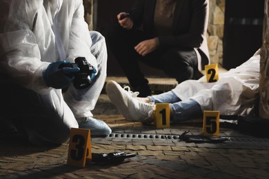 Photo of Investigator and criminologist working at crime scene with dead body outdoors, closeup