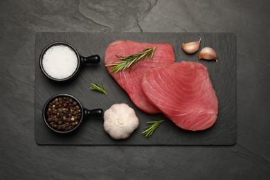 Photo of Fresh raw tuna fillets with rosemary and spices on black table, top view