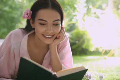 Beautiful young woman reading book in park on sunny day