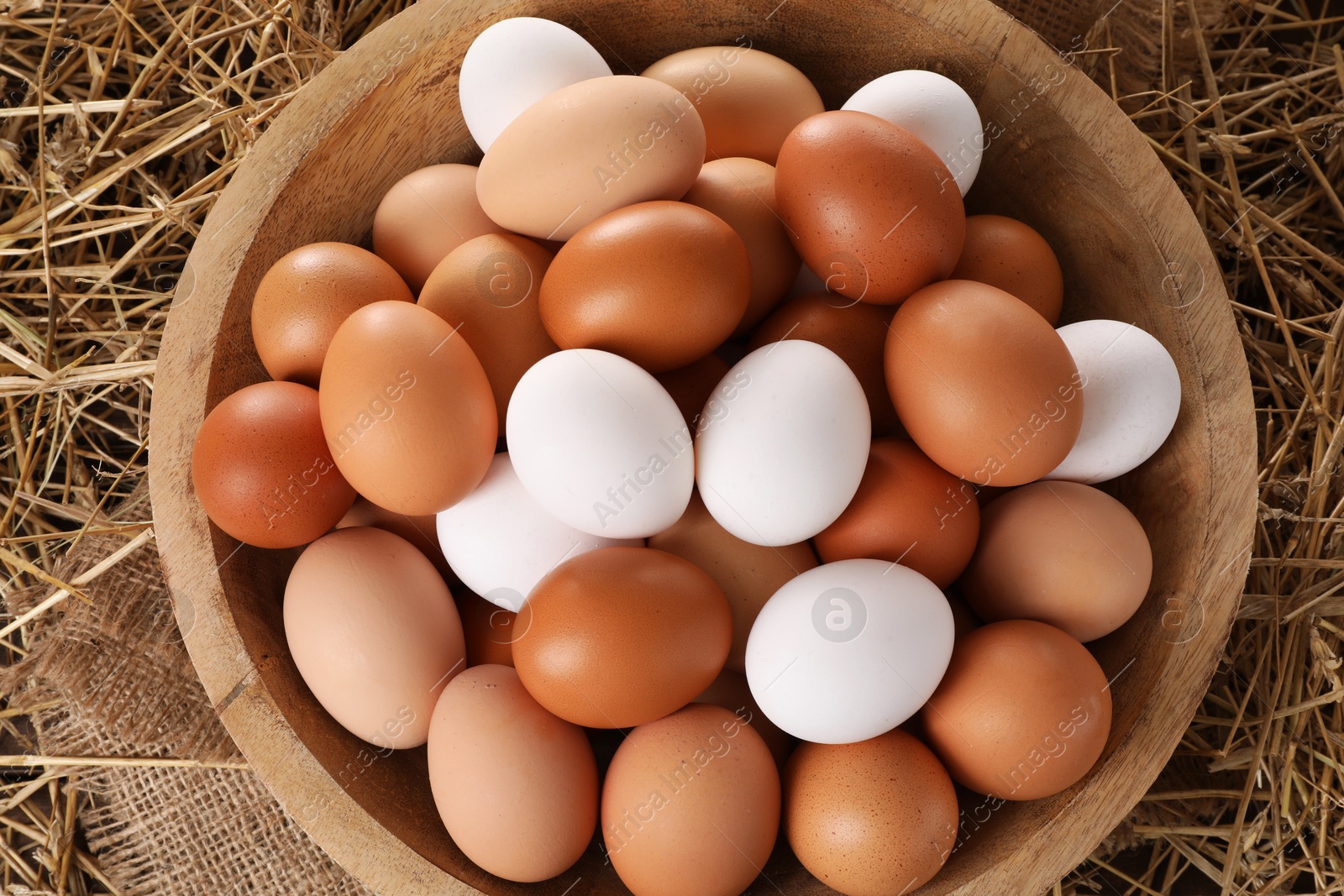 Photo of Fresh chicken eggs in bowl on dried straw, top view