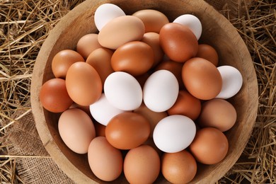 Fresh chicken eggs in bowl on dried straw, top view