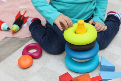 Photo of Little child playing with stacking toy on carpet, closeup