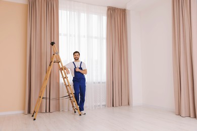 Worker in uniform showing thumbs up near window curtains indoors