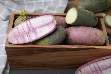 Photo of Purple and green daikon radishes in crate on black wooden table