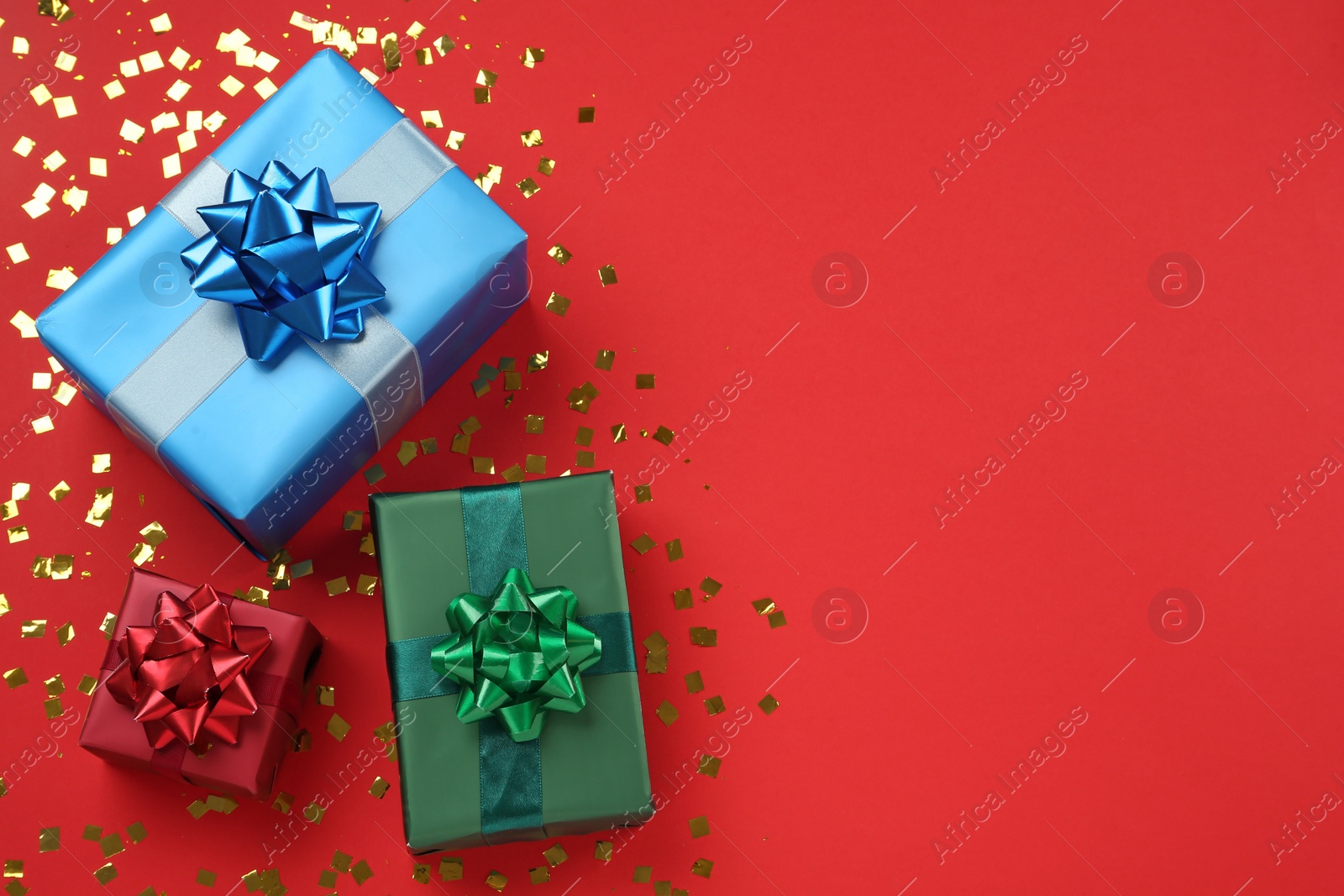 Photo of Gift boxes and shiny confetti on red background, flat lay. Space for text