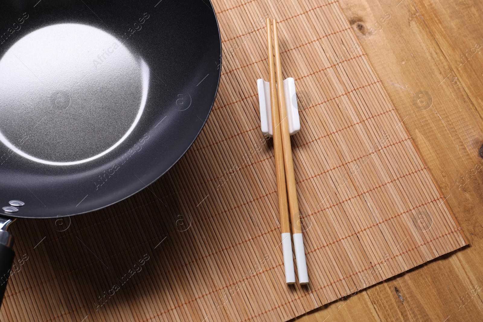 Photo of Empty iron wok and chopsticks on wooden table, closeup