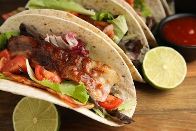 Photo of Delicious tacos with fried bacon and lime on wooden table, closeup