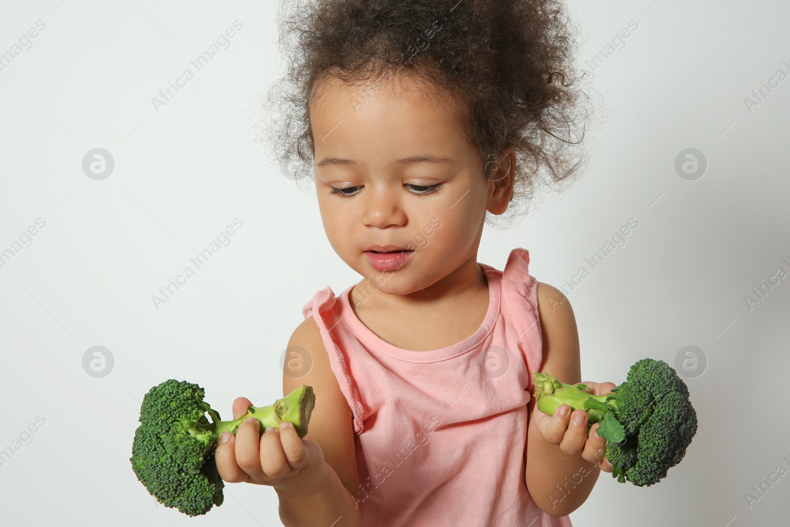 Photo of Cute African-American girl with broccoli on white background